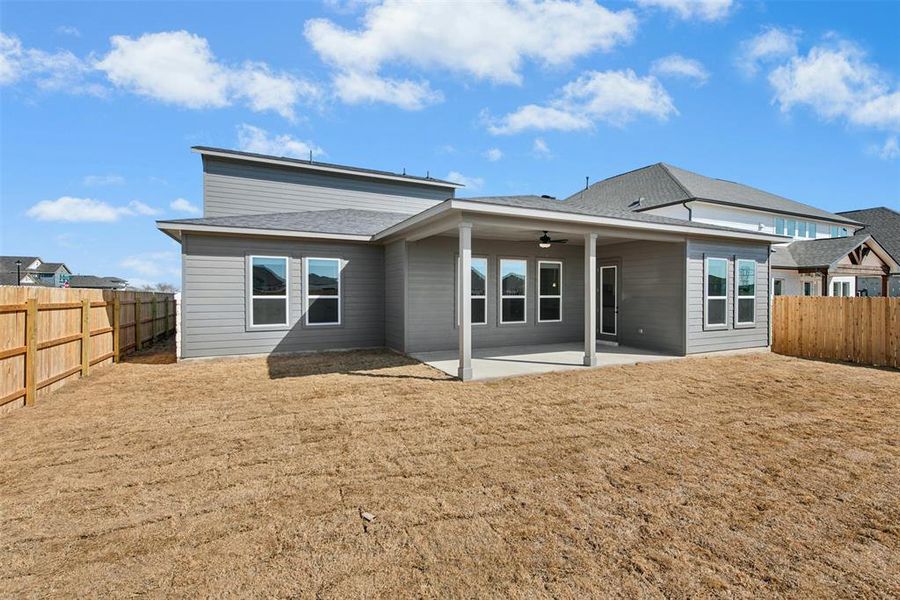Expansive backyard featuring a covered patio with a ceiling fan, multiple windows, and a wood privacy fence