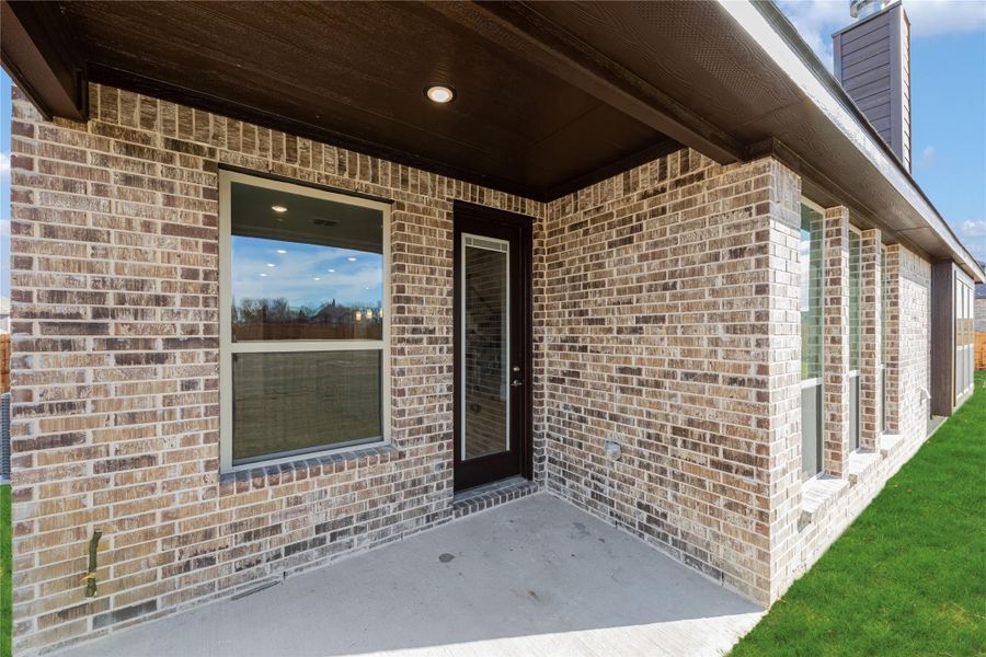 Covered back patio with brick exterior, black door, and concrete slab next to green lawn Covered back patio with brick exterior, black door, and concrete slab next to green lawn