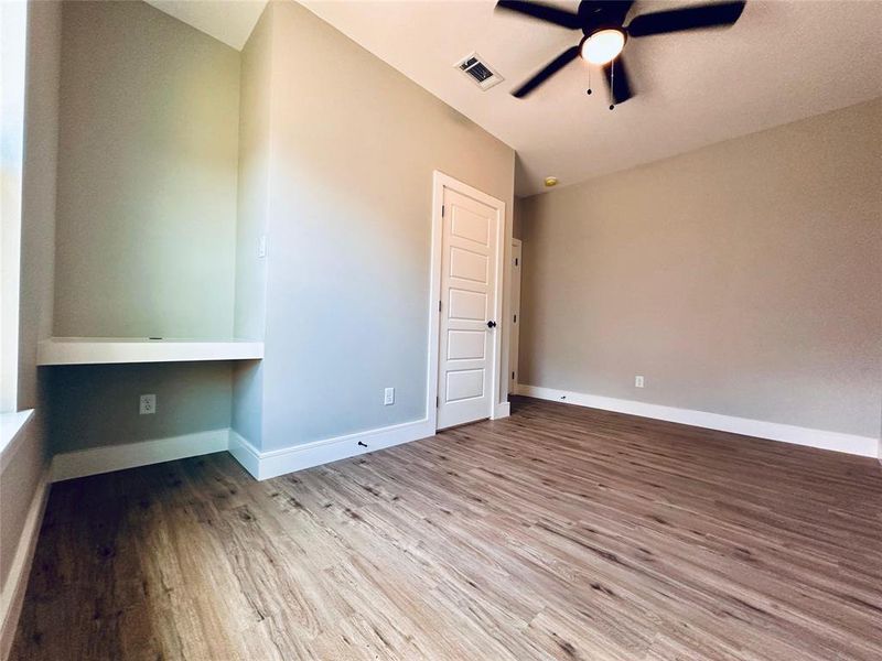 Secondary bedroom with built-in desk, closet and ceiing fan.