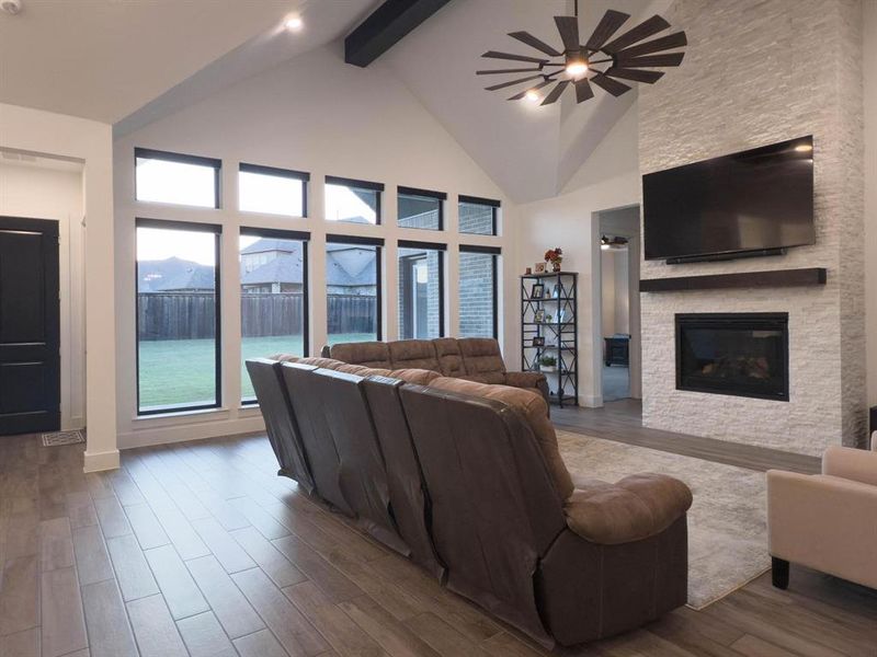 Living room featuring high vaulted ceiling, wood finished floors, beam ceiling, a stone fireplace, and ceiling fan Living room featuring high vaulted ceiling, wood finished floors, beam ceiling, a stone fireplace, and ceiling fan