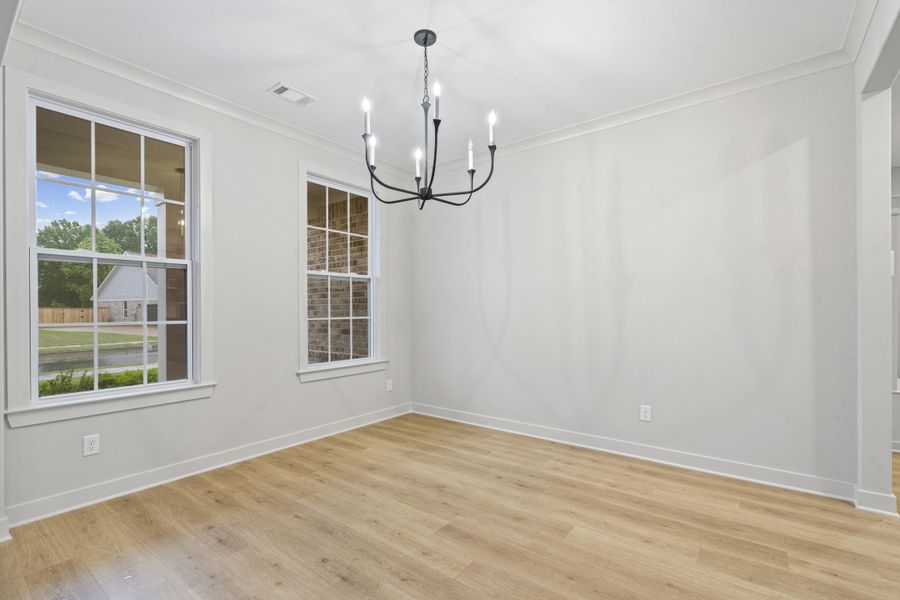 Spacious room with wood-finish flooring, featuring a black chandelier and white trim Spacious room with wood-finish flooring, featuring a black chandelier and white trim