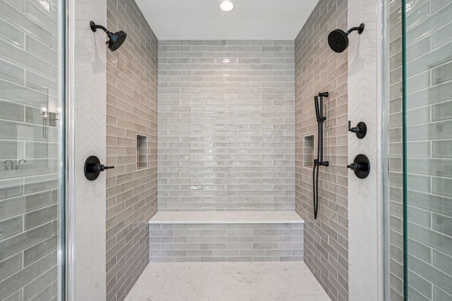 This photo showcases a spacious, modern shower with dual showerheads, elegant gray tile, built-in niches for storage, and a convenient bench.