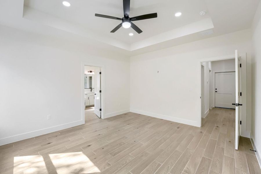 Recessed lighting and a modern ceiling fan illuminate this roomy bedroom with wood-plank flooring.