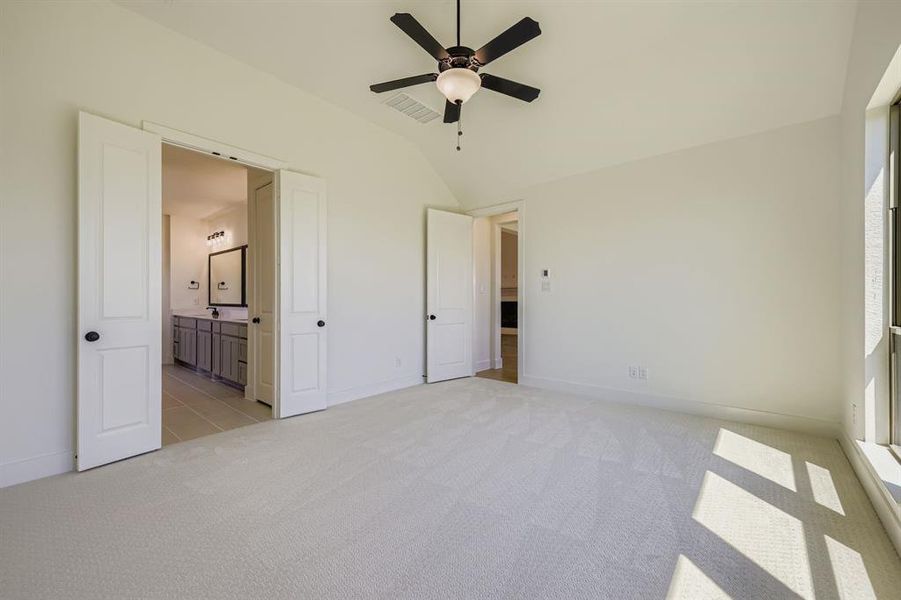 Unfurnished bedroom with light carpet, lofted ceiling, ceiling fan, and ensuite bath Unfurnished bedroom with light carpet, lofted ceiling, ceiling fan, and ensuite bath