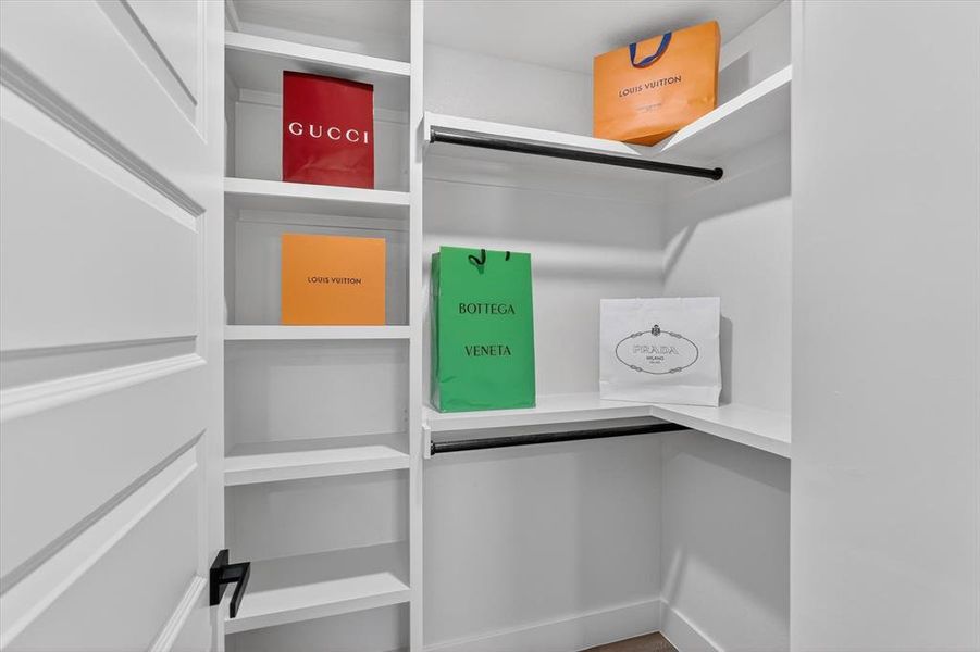 Walk-in closet featuring white built-in shelving, hanging rods with a matte black finish, and a paneled door with a matte black lever handle