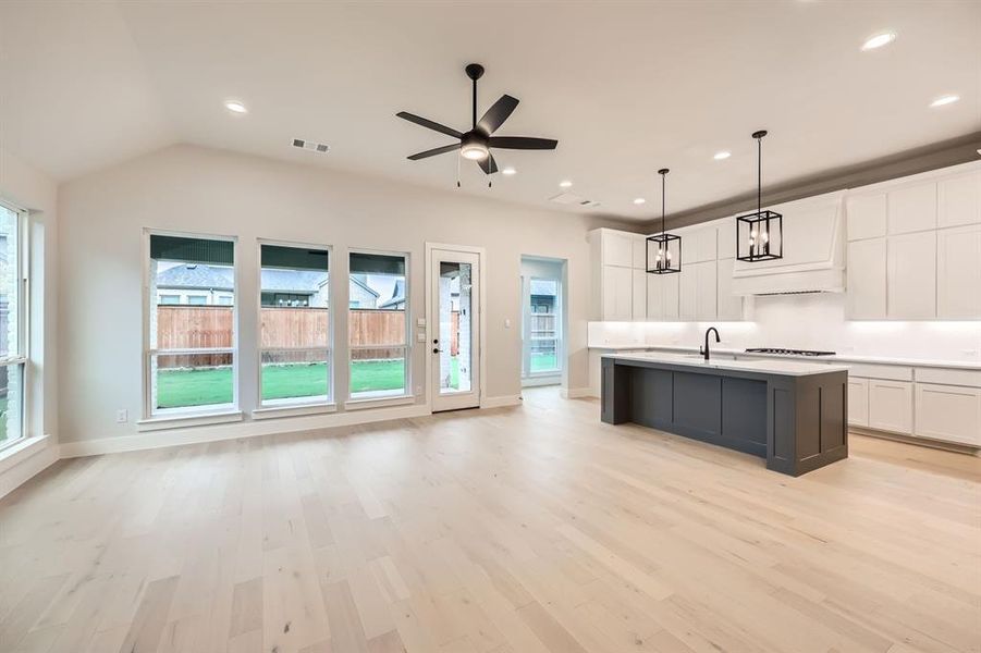 Kitchen with decorative light fixtures, an island with sink, light hardwood / wood-style floors, and white cabinets