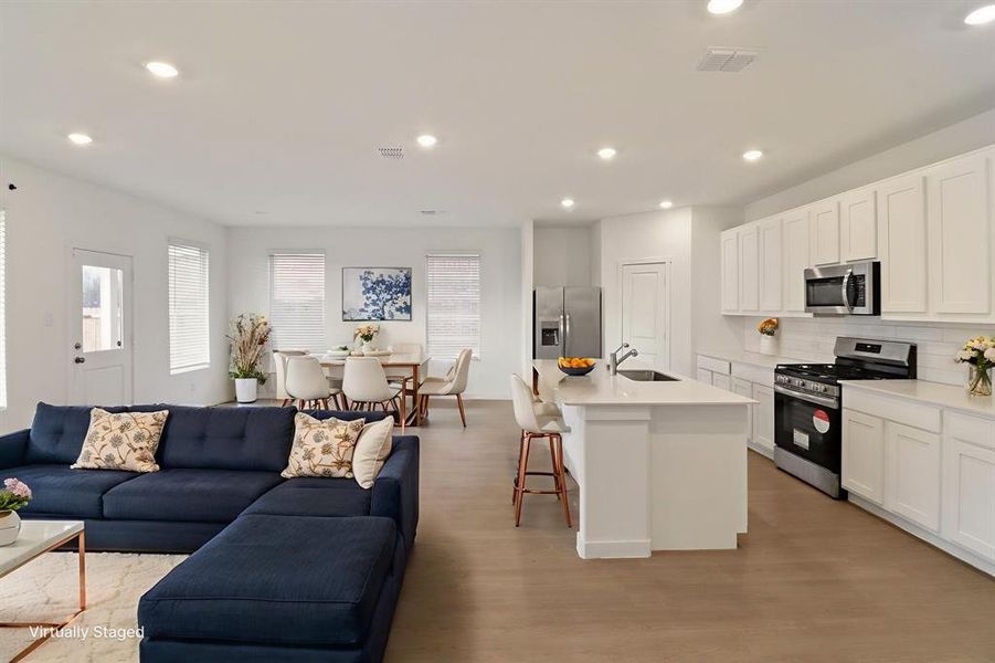 Kitchen with open floor plan, stainless steel appliances, a breakfast bar area, recessed lighting, and an island with sink