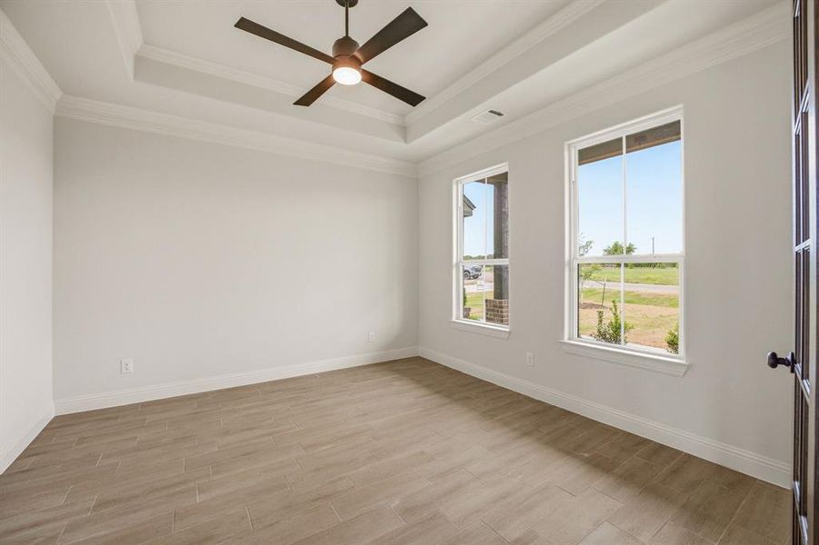 Empty room with a ceiling fan, light wood finished floors, a tray ceiling, and crown molding