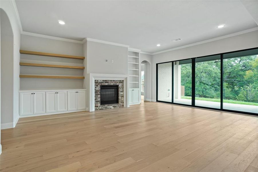 Unfurnished living room with built in features, a fireplace, light hardwood / wood-style flooring, and ornamental molding