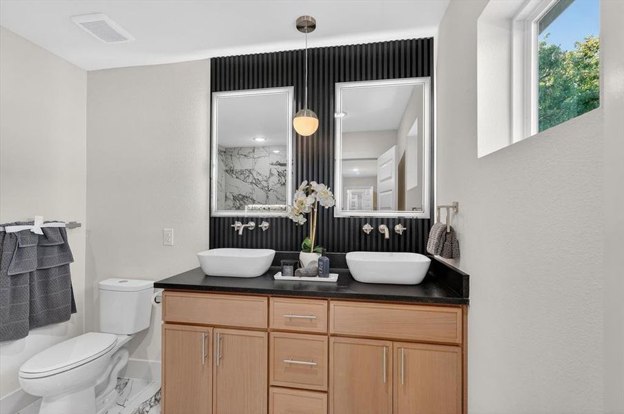 Bathroom vanity featuring dual vessel sinks, a dark countertop, and light wood-finish cabinetry