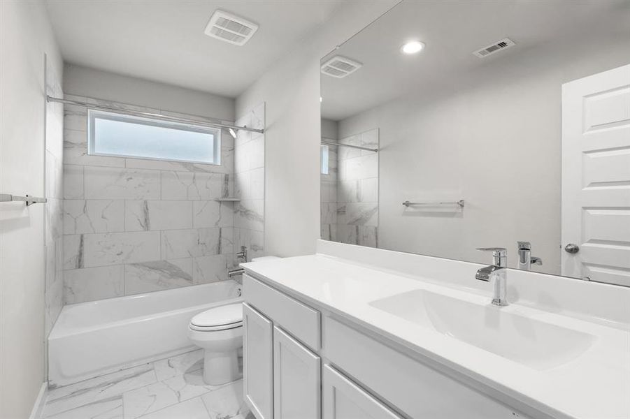 Indulge in refined charm in the secondary bathroom, where the tile flooring harmonizes with a bath/shower combo surrounded by tasteful tile. Light wood cabinets, coupled with a gorgeous countertop, elevate the space, cultivating a truly welcoming atmosphere. Sample photo of completed home with similar floor plan. As-built interior colors and selections may vary.