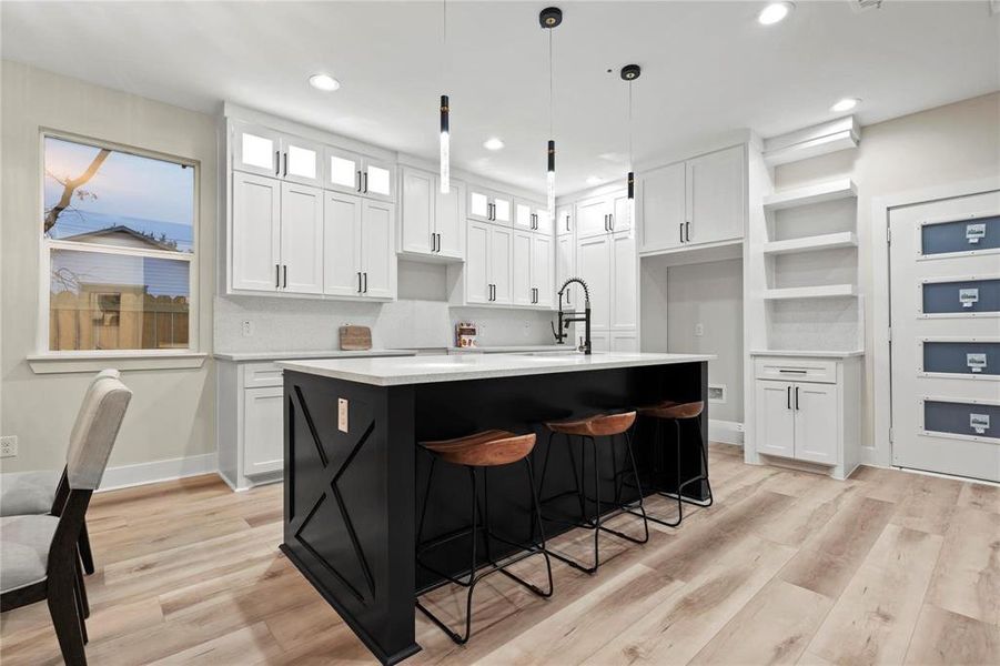 Dual tone kitchen featuring light wood-style floors, hanging light fixtures, a kitchen island with sink, a kitchen bar, and two tone color scheme Dual tone kitchen featuring light wood-style floors, hanging light fixtures, a kitchen island with sink, a kitchen bar, and two tone color scheme