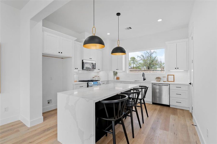 Adding character to the kitchen is an oversized rectangular window positioned above the sink, allowing natural light to flood the space, while soft close cabinets and drawers align along two sides, maximizing storage and functionality with a touch of elegance.