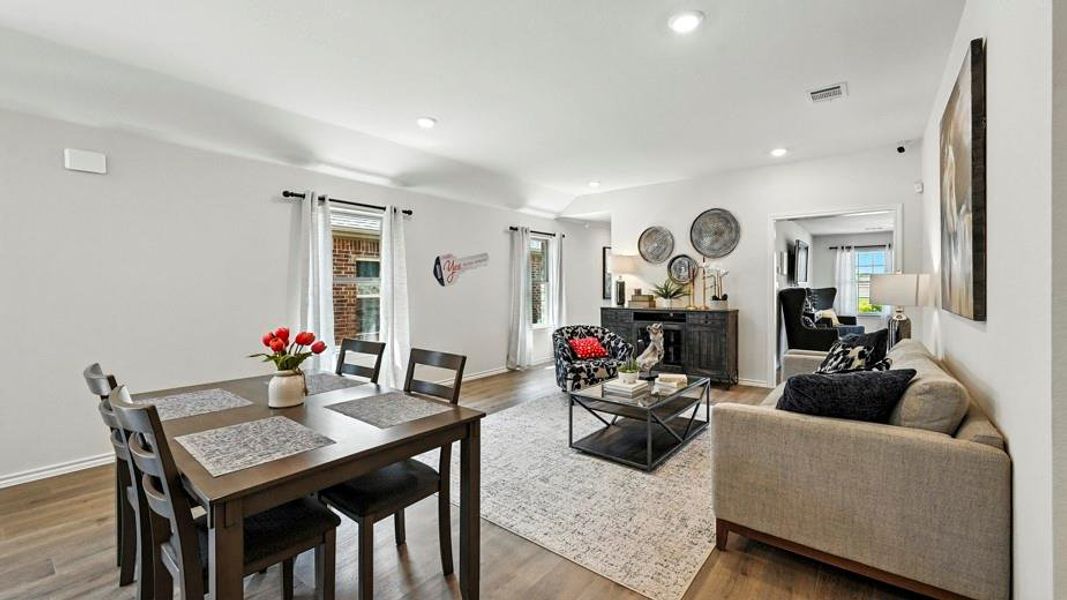 Bright, open-concept living and dining area featuring wood-finish flooring, recessed lighting, and white interior walls