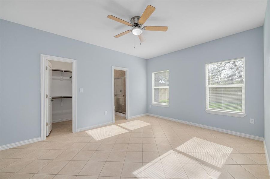 Unfurnished bedroom with a spacious closet, ceiling fan, ensuite bathroom, a closet, and light tile patterned floors