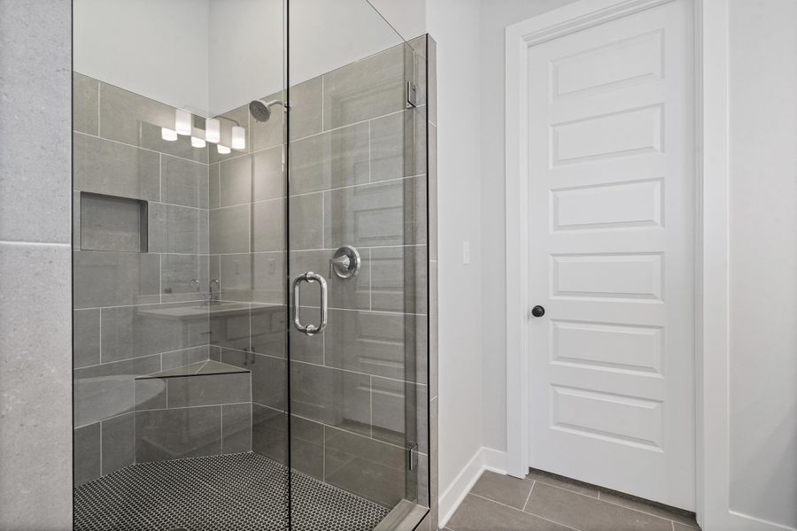 Glass-enclosed shower featuring large format gray wall tiling, a built-in corner bench, a recessed shower niche, and a circular mosaic tile floor Glass-enclosed shower featuring large format gray wall tiling, a built-in corner bench, a recessed shower niche, and a circular mosaic tile floor