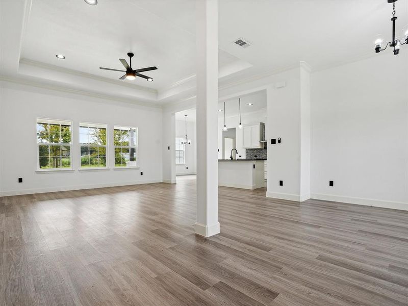 Unfurnished living room featuring ceiling fan with notable chandelier, light wood-type flooring, sink, and a raised ceiling