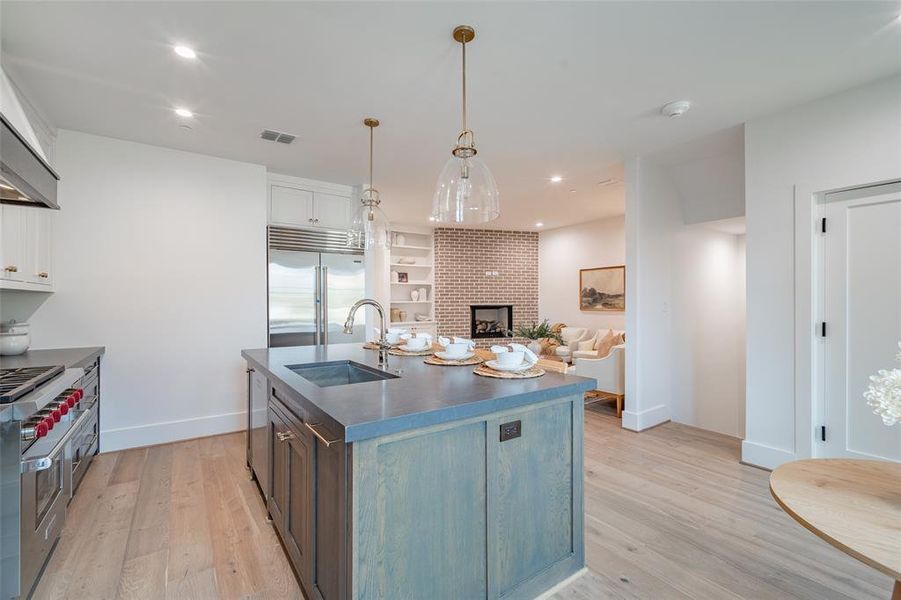 Kitchen with white cabinetry, sink, light hardwood / wood-style flooring, a kitchen island with sink, and high end appliances