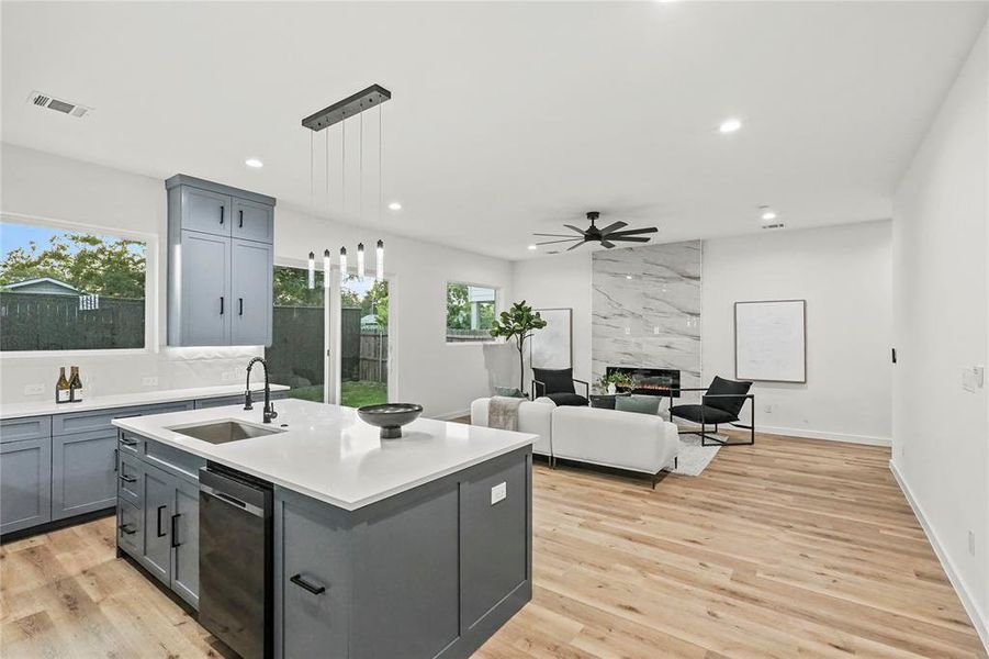 Kitchen with dishwashing machine, ceiling fan, an island with sink, sink, and light hardwood / wood-style flooring