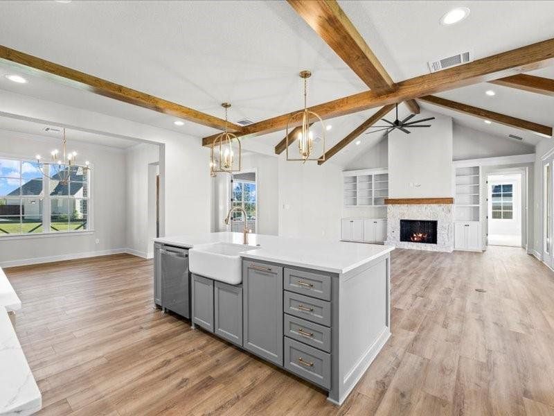 Kitchen featuring gray cabinetry, open floor plan, decorative light fixtures, a lit fireplace, and a kitchen island with sink Kitchen featuring gray cabinetry, open floor plan, decorative light fixtures, a lit fireplace, and a kitchen island with sink