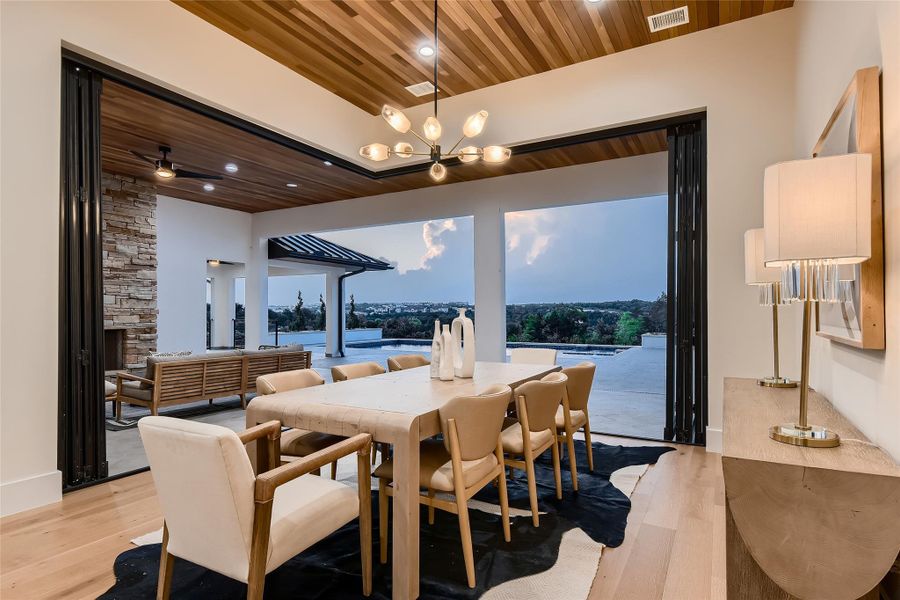 Dining area featuring light wood flooring, a decorative ceiling, and an expansive opening to an outdoor living space with a stone fireplace