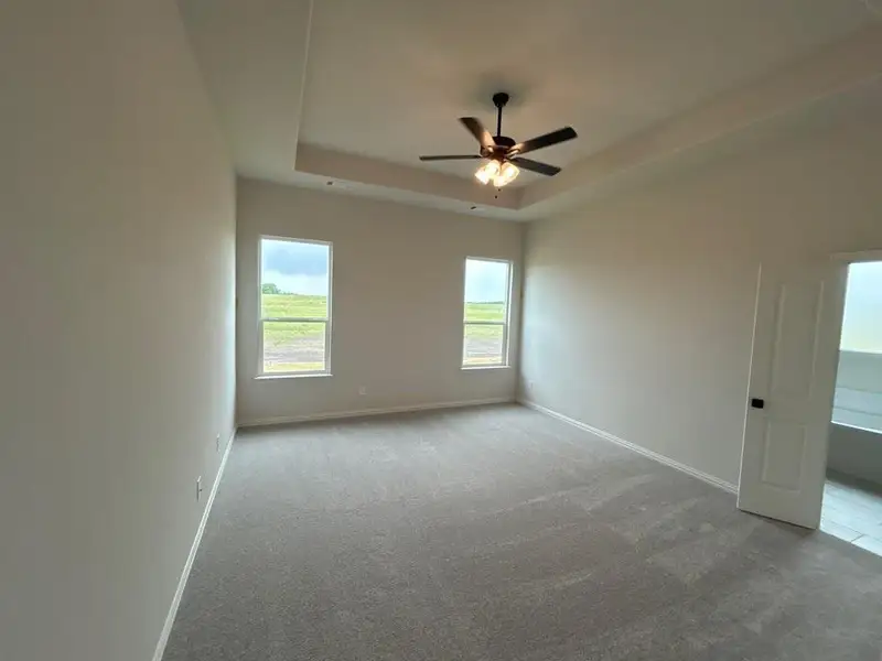 Spacious room featuring a tray ceiling with a ceiling fan, two windows, and light-colored carpeting