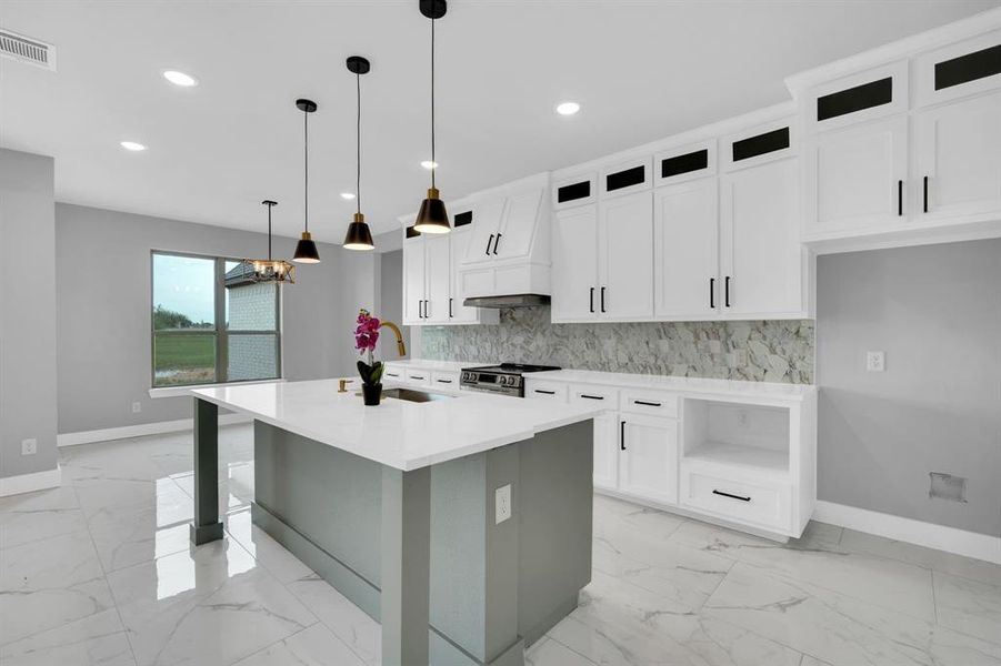 Kitchen featuring stainless steel range, decorative light fixtures, an island with sink, tasteful backsplash, and sink