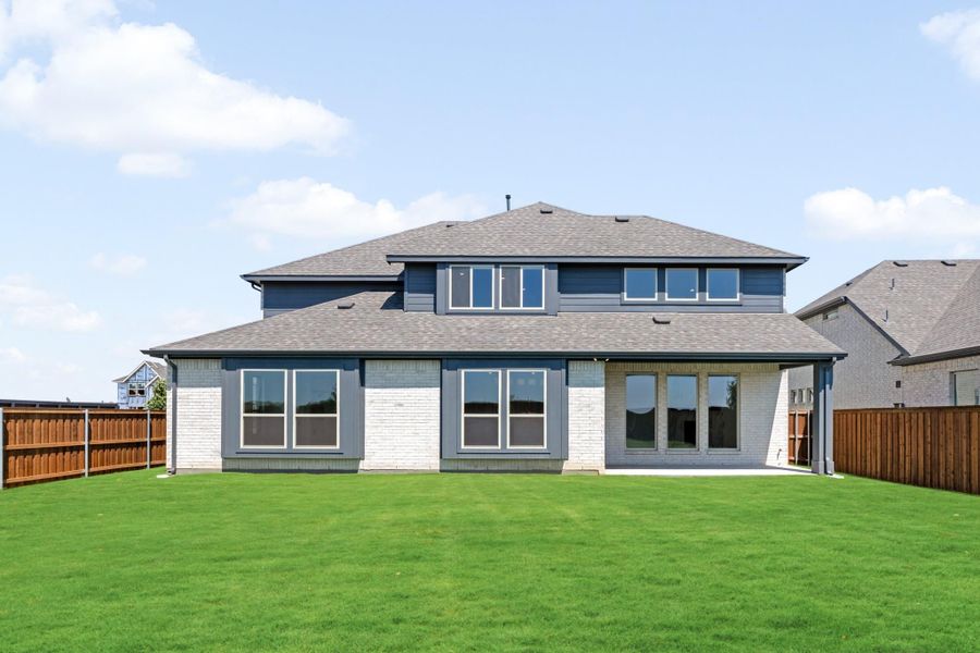 Two-story home rear exterior with gray and white brick, large windows, patio doors, and fenced backyard lawn