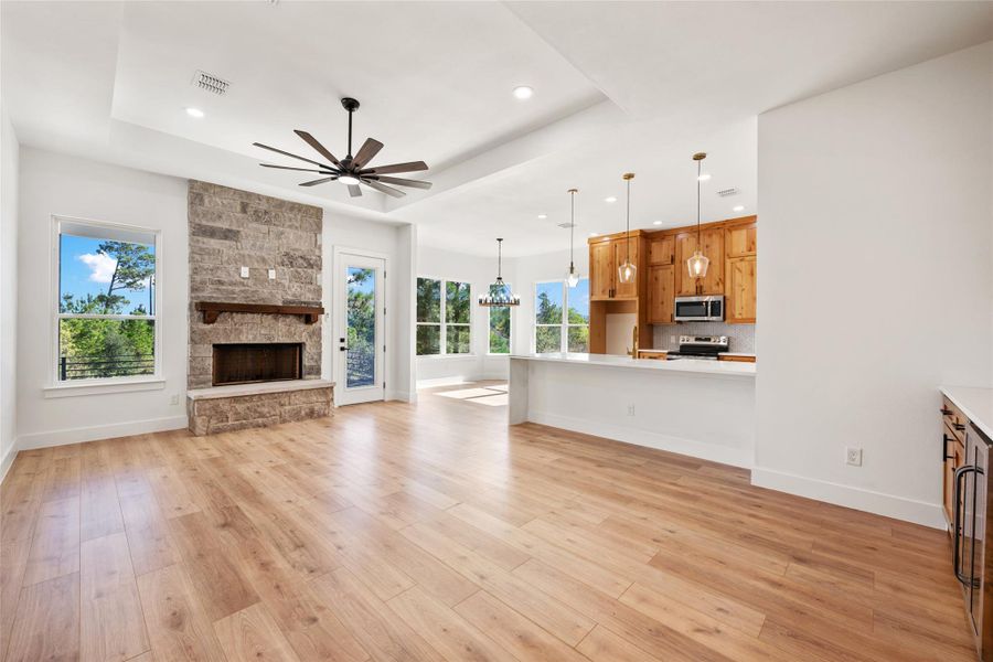 Unfurnished living room featuring light wood-style floors, a ceiling fan, a stone fireplace, a chandelier, and a raised ceiling
