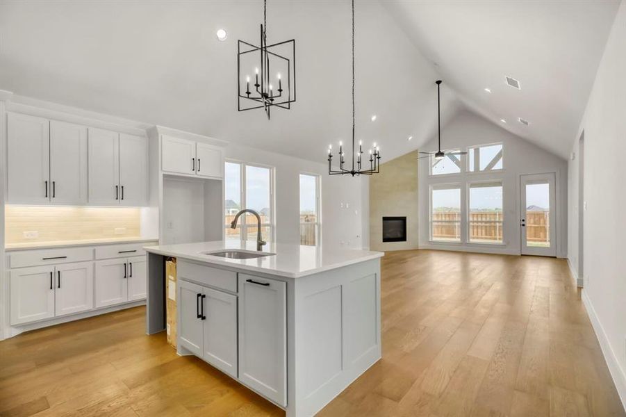 Kitchen featuring white cabinetry, a large fireplace, an island with sink, light wood-style floors, and a chandelier