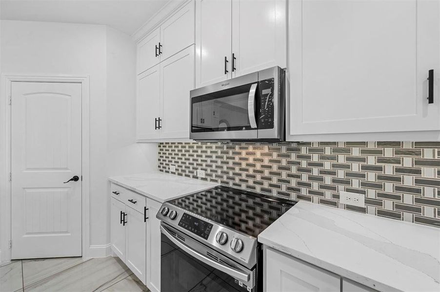 Kitchen featuring light tile patterned floors, appliances with stainless steel finishes, decorative backsplash, light stone counters, and white cabinets