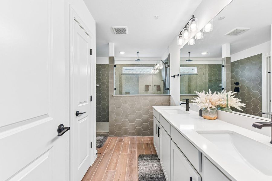 Modern bathroom featuring dual vanities, a spacious walk-in shower with hexagonal tile accents, and warm wood-look flooring.