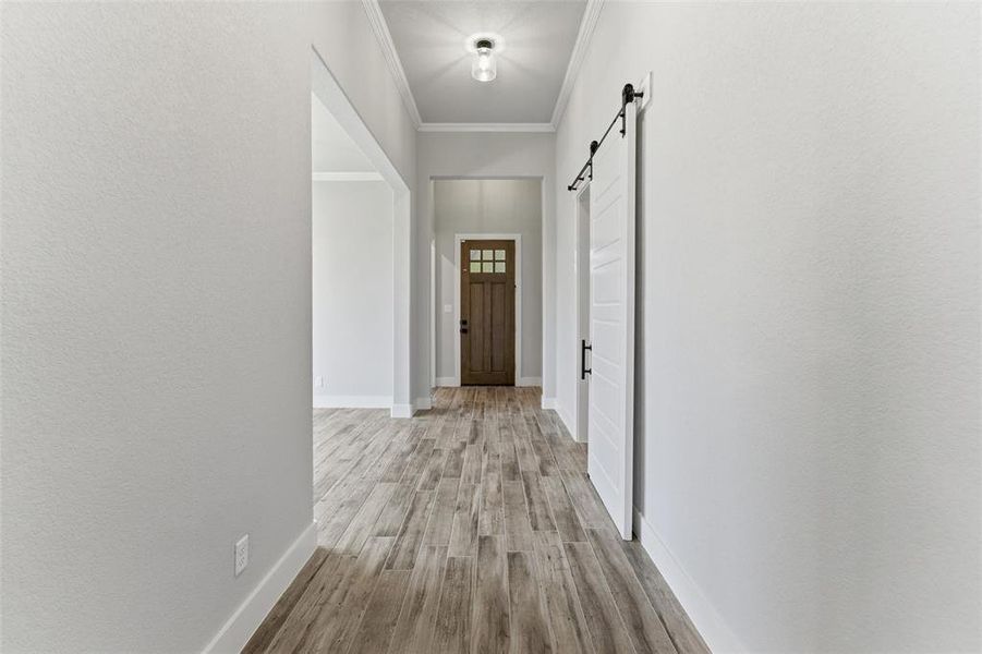 Hallway featuring wood-finish flooring, a white paneled barn door with black hardware, white baseboards, and a recessed ceiling light fixture