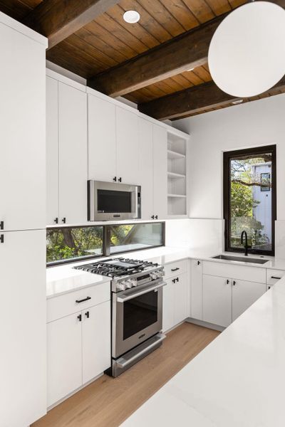 Kitchen with open shelves, white cabinetry, stainless steel appliances, light wood-style flooring, and a wood ceiling with exposed beams