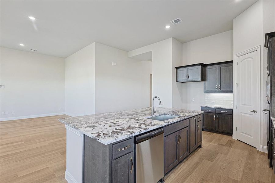 Kitchen featuring stainless steel appliances, an island with sink, light stone countertops, light wood-style floors, and recessed lighting