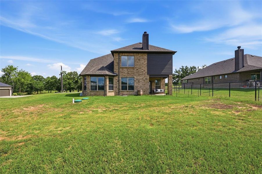 Expansive rear yard featuring a brick and siding exterior, multiple large windows, and a covered patio area