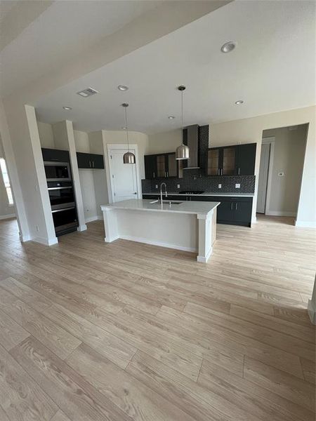 Kitchen featuring sink, backsplash, an island with sink, extractor fan, and light wood-type flooring