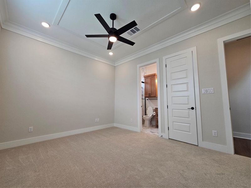 This is a bright, carpeted bedroom with a modern black ceiling fan and recessed lighting. It features a door leading to an en-suite bathroom with a visible toilet and wooden cabinetry. The room has a neutral color palette, creating a clean and inviting space. This is a bright, carpeted bedroom with a modern black ceiling fan and recessed lighting. It features a door leading to an en-suite bathroom with a visible toilet and wooden cabinetry. The room has a neutral color palette, creating a clean and inviting space.