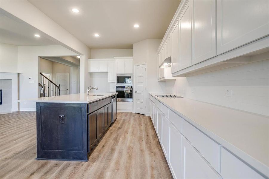 Kitchen with appliances with stainless steel finishes, a kitchen island with sink, sink, light hardwood / wood-style floors, and white cabinetry