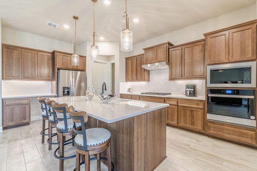 Kitchen with visible vents, appliances with stainless steel finishes, brown cabinetry, a sink, and a kitchen breakfast bar