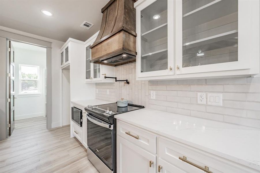 Kitchen with glass insert cabinets, white cabinetry, electric stove, premium range hood, and light stone counters