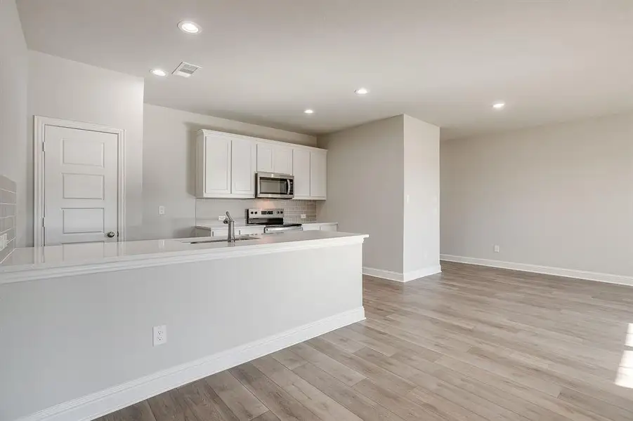 Kitchen with white cabinets, stainless steel appliances, light wood-type flooring, recessed lighting, and light stone countertops