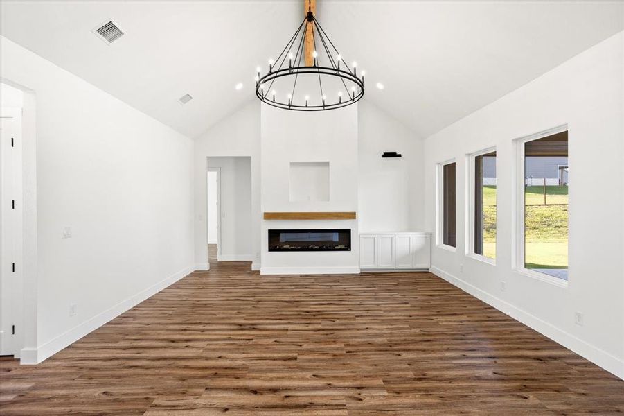 Unfurnished living room with high vaulted ceiling, dark wood finished floors, a glass covered fireplace, and a chandelier Unfurnished living room with high vaulted ceiling, dark wood finished floors, a glass covered fireplace, and a chandelier
