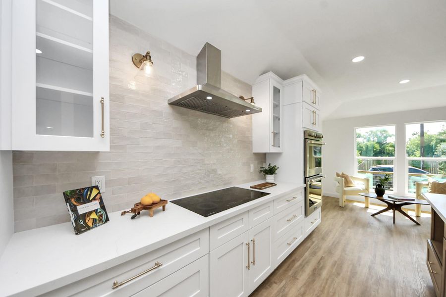 A beautifully curated kitchen where modern white cabinetry with glass accents meets warm brass hardware and soft, ambient lighting. The sleek induction cooktop and stainless steel range hood offer a streamlined look, while a beige subway tile backsplash brings just the right touch of warmth and texture. A beautifully curated kitchen where modern white cabinetry with glass accents meets warm brass hardware and soft, ambient lighting. The sleek induction cooktop and stainless steel range hood offer a streamlined look, while a beige subway tile backsplash brings just the right touch of warmth and texture.