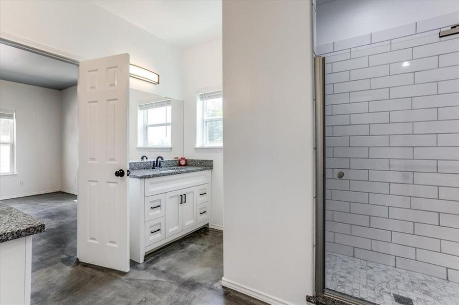 Bathroom featuring a double vanity with stone countertop, white cabinetry with dark hardware, and a fully enclosed shower with subway tile surround and mosaic floor