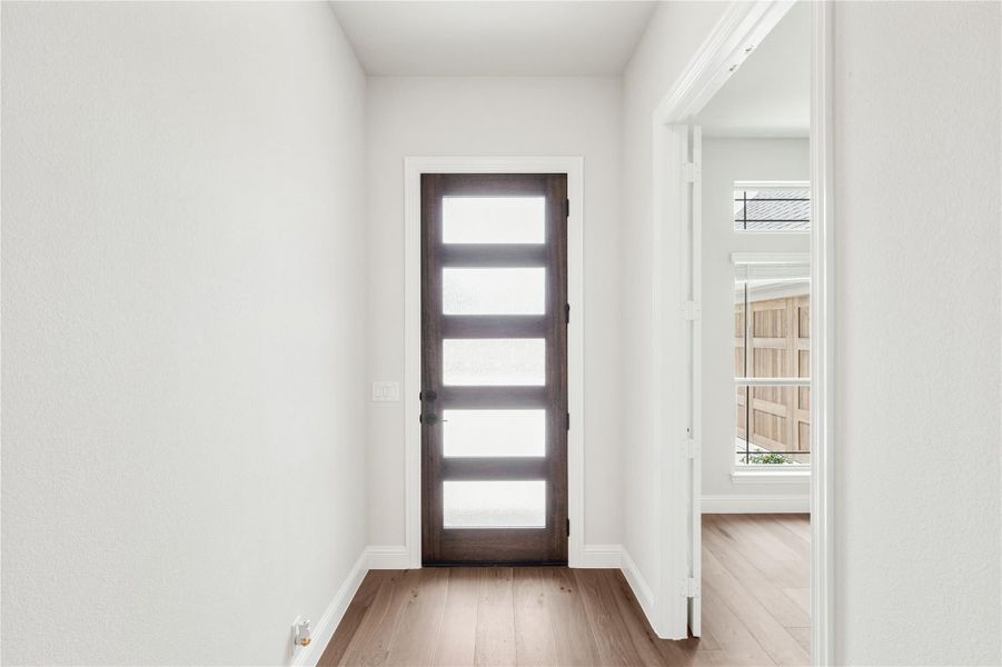 Entryway hallway with dark wood glass-panel door and light hardwood floors