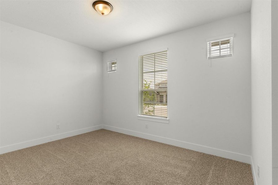 Carpeted interior space featuring neutral wall paint, white trim, multiple windows with blinds, and an overhead light fixture Carpeted interior space featuring neutral wall paint, white trim, multiple windows with blinds, and an overhead light fixture