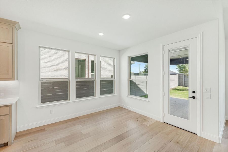 Bright dining nook with light wood floors, three windows, and glass back door leading to backyard Bright dining nook with light wood floors, three windows, and glass back door leading to backyard