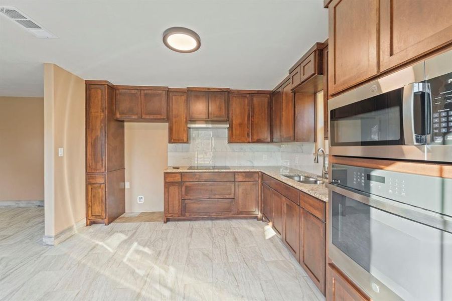 Kitchen with appliances with stainless steel finishes, light stone counters, tasteful backsplash, and brown cabinets Kitchen with appliances with stainless steel finishes, light stone counters, tasteful backsplash, and brown cabinets