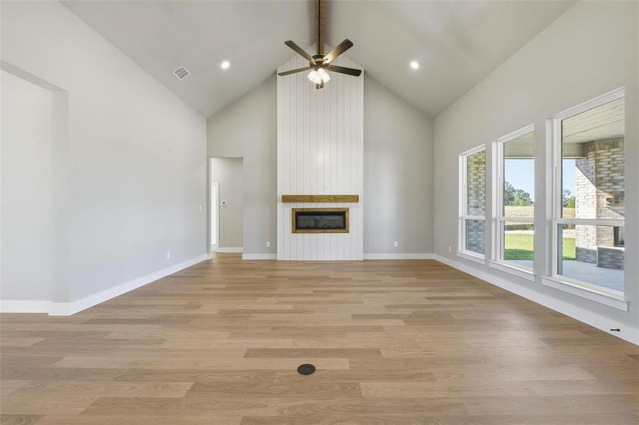 Unfurnished living room with high vaulted ceiling, beamed ceiling, light wood-style floors, a large fireplace, and a ceiling fan